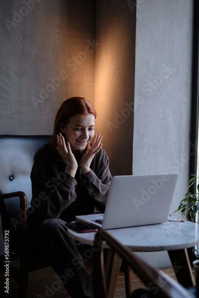 Fototapeta red-haired woman freelancer works remotely on laptop in cafe.