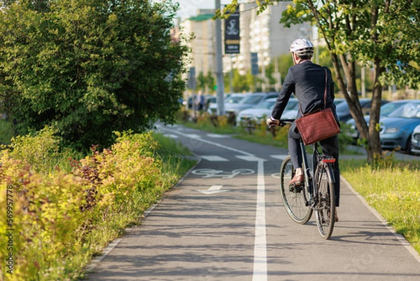 Obraz Stylish businessman in helmet cycling on bike path in sunny day.