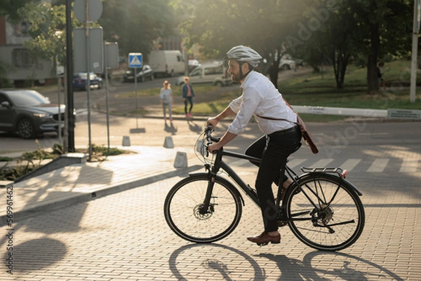 Obraz Smiling bearded entrepreneur riding on bike on street in morning.