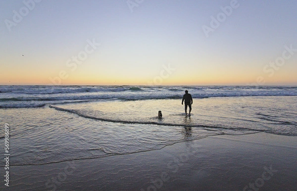 Obraz hombre jugando con su perro pug en la orilla del mar mientras esta la puesta de sol