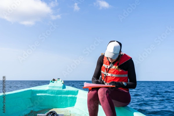 Fototapeta Marine biologist writing down data sitting on a boat