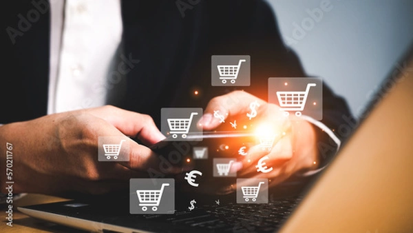 Obraz Businessman holding phone and laptop used for online shopping through websites on the Internet, Selective focus of small shopping bags near toy shopping trolley with laptop on background.
