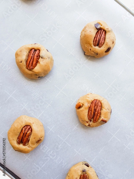 Fototapeta Homemade brown butter cookies with pecan nuts and milk chocolate on a tray and a parchment paper. Photo in process.