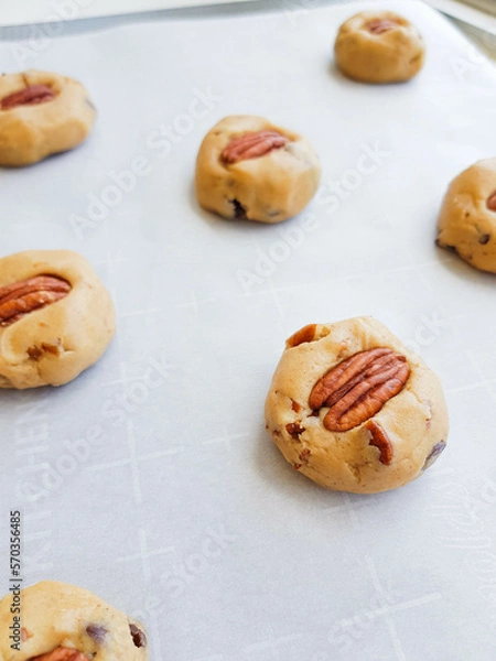 Fototapeta Homemade brown butter cookies with pecan nuts and milk chocolate on a tray and a parchment paper. Photo in process.