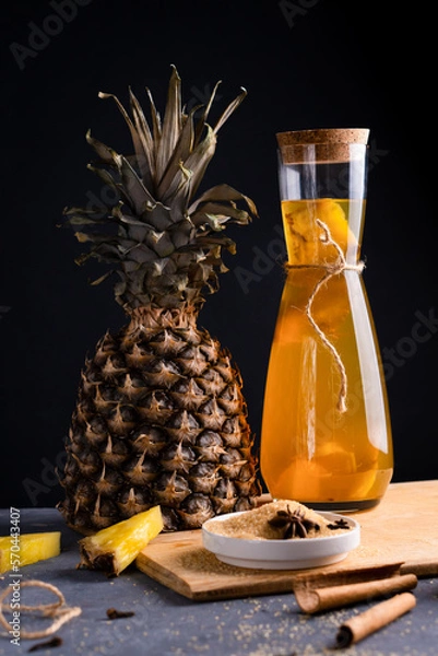 Fototapeta Pineapple Tepache. Fermented drink from pineapple served in bottle in low key. Dark background.