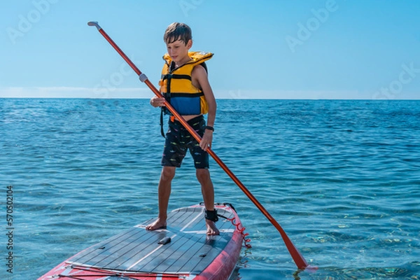 Obraz A 9-year-old white boy from Eastern Europe learns to paddleboard in the sea. Front view