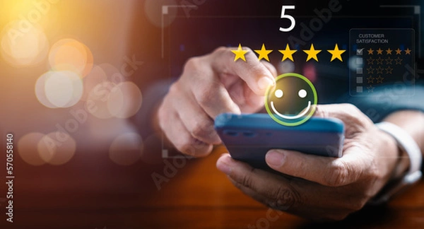 Fototapeta Businessman use smartphone to give five star rating on virtual screen by touching happy face icon
