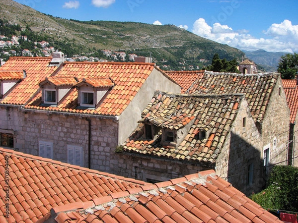 Fototapeta A charming view of several terra cotta coloured rooftops in Dubrovnik, Croatia on a sunny day with a blue sky with clouds as a backdrop.  Image has copy space.