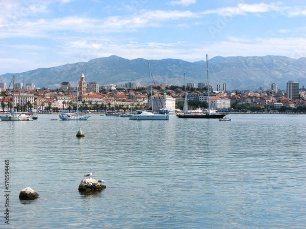 Fototapeta Boats off the coast of Split, Croatia with the city and mountains behind them on a sunny day with a blue, cloudy sky.  Image has copy space.