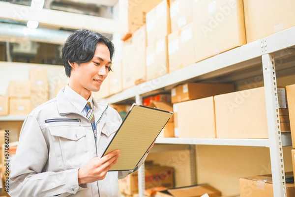 Obraz 作業服を着て倉庫で在庫管理をする若いビジネスマン