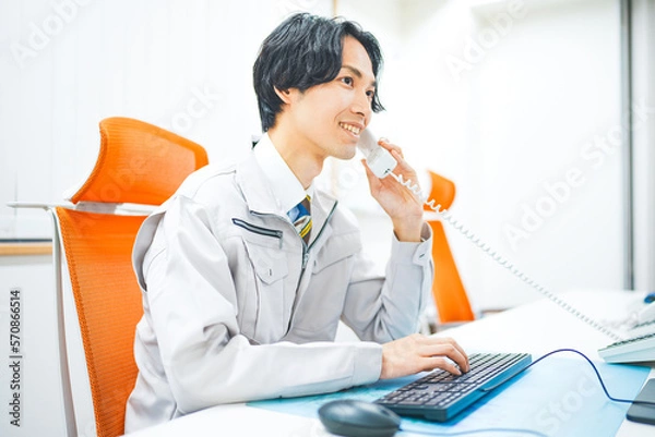 Obraz 作業着を着て電話応対をする若いエンジニアの男性