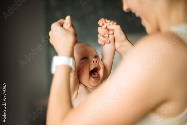 Fototapeta Blurred of a faceless loving mother, looking at her little son and holding his hands while playing and doing exercise, having free time together