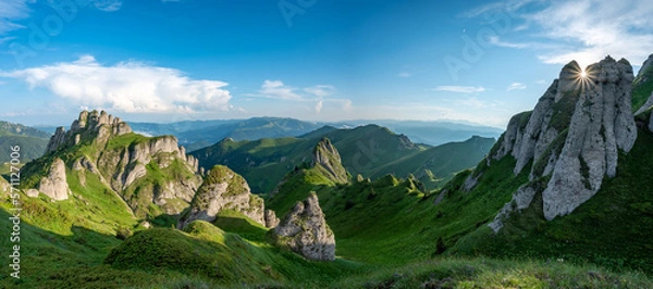 Fototapeta Panorama of green meadow with rocks and rocky mountains in romanian mountains in muntii ciucas with setting sun