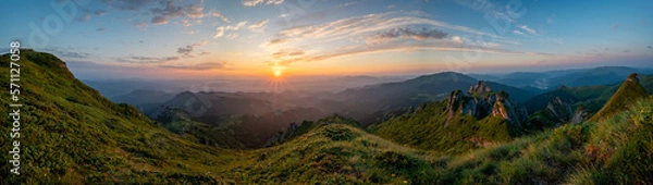 Fototapeta Panorama of green meadow with rocks and rocky mountains in romanian mountains in muntii ciucas with raising sun