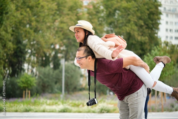 Fototapeta Multiracial couple of tourists piggyback with spread arms like plane wings. Sightseeing in Madrid, Spain.