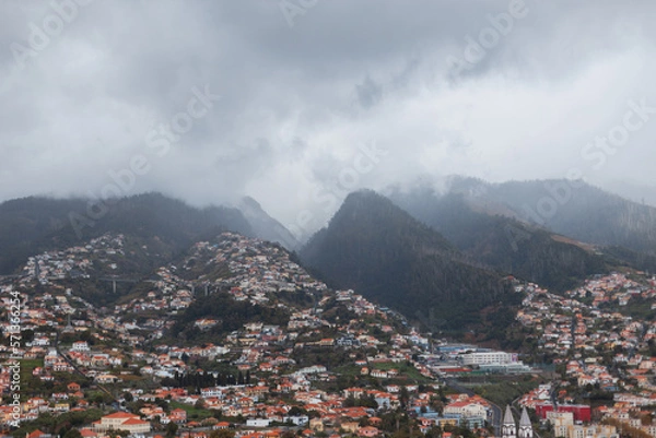 Fototapeta Beautiful mountains with fog, clouds and houses on Madeira island. City on the side of a mountain
