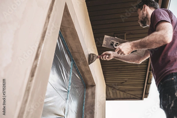 Obraz Renovation of the building facade - construction industry. Worker man plastering exterior walls of a house.