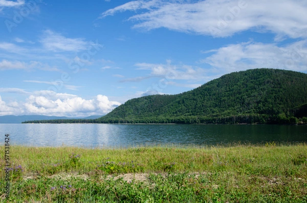 Fototapeta Bay on Lake Baikal in sunny summer weather. In the smooth water, clouds and mountains covered with forest are reflected.