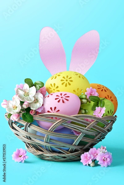 Fototapeta Multi colors Easter eggs in the basket with bunny ears and flowers on blue background. Pastel color Easter eggs.