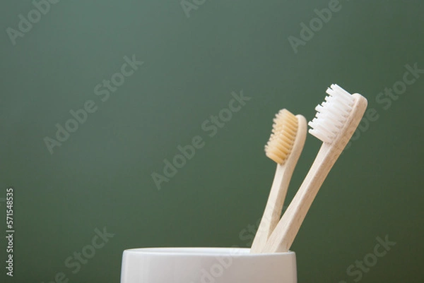Fototapeta Two wooden bamboo toothbrushes in a white glass on a green background. The concept of sustainability and the rejection of plastic. The concept of hygiene and daily routine. Copy spase, close-up