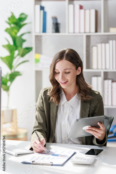 Fototapeta Concept of business investment or working woman,  Businesswoman wearing a suit sitting and working on analysis of business investment documents and using tablet to analytic business data.