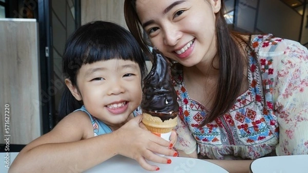 Obraz both mother and her daughter were trying to bite and enjoying the chocolate ice cream cone they had just bought from the shop