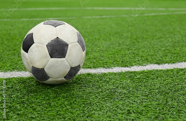 Fototapeta Dirty soccer ball on green football field, space for text