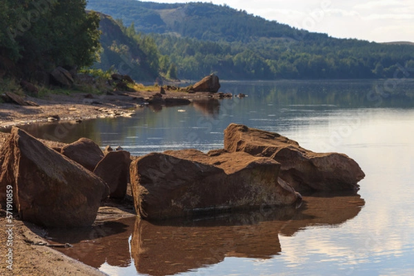 Fototapeta lake surrounded by green forest, hill with forest on background.Summer day.Large rock in water