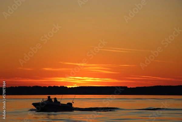 Fototapeta Silhouette of two fisherman on the boat. Beautiful sunset on the background.