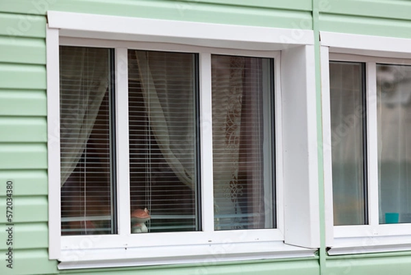 Fototapeta White window openings of plastic windows with an external facade of green siding