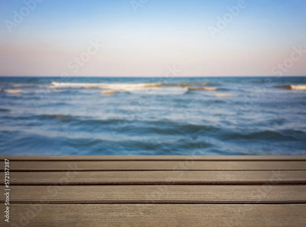 Fototapeta Natural, abstract, unfocused background. Seascape. An empty wooden base, a wooden table, a tabletop against the background of sunset, dawn on the seashore. Copy space