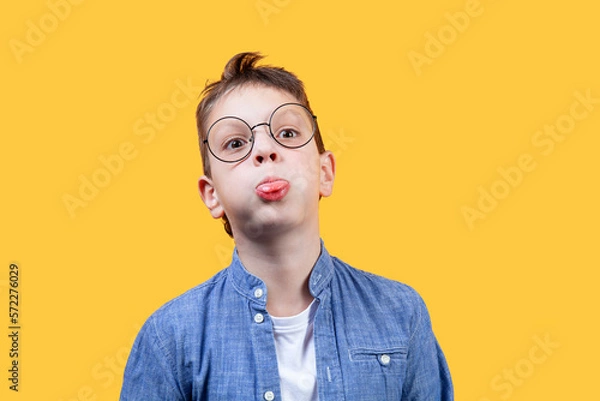 Obraz Portrait of a boy with glasses. He fools around and sticks out his tongue. Front view. Yellow background. Suitable for collage and banner making and other design