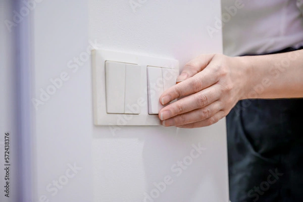 Obraz A woman turns off the home light switch when she leaves the room. Power, energy saving, energy saving.