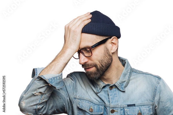 Fototapeta Horizontal portrait of stressful stylish unshaven male regrets something, keeps hand on head, looks down in despair, isolated over pink background. European man recieves failure, poses indoor