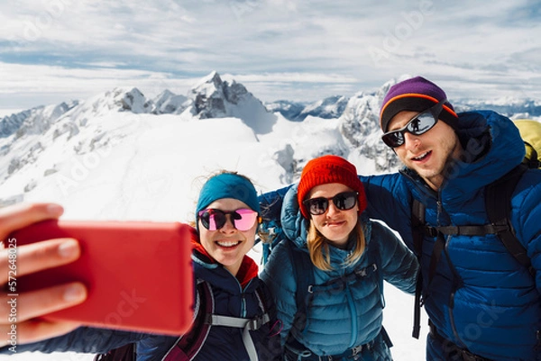 Fototapeta Woman hiker taking a selfie of the group while on top of the mountain on a sunny winter day
