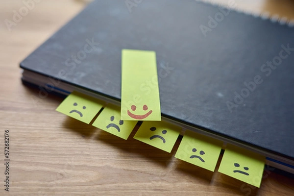 Fototapeta Lachende und traurige Gesichter auf post it Zettel in einem Notizbuch auf einem Schreibtisch aus Holz. 