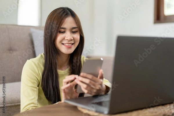 Fototapeta Young woman is sitting to smiling on the floor and using laptop