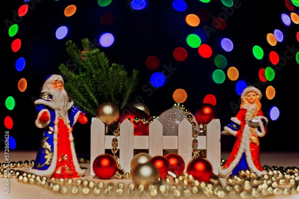 Fototapeta Christmas card with Santa Claus,Snow Maiden.Christmas tree. on a dark background with bright flashing lights of garlands.A statuette, a Santa Claus toy.Christmas tree toys on the Christmas tree. bokeh