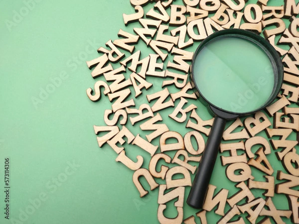 Obraz Wooden word and magnifying glass on a green background