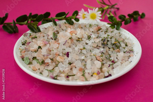 Obraz herbal salt on a white plate on a pink background with flowers and green leafs, close up