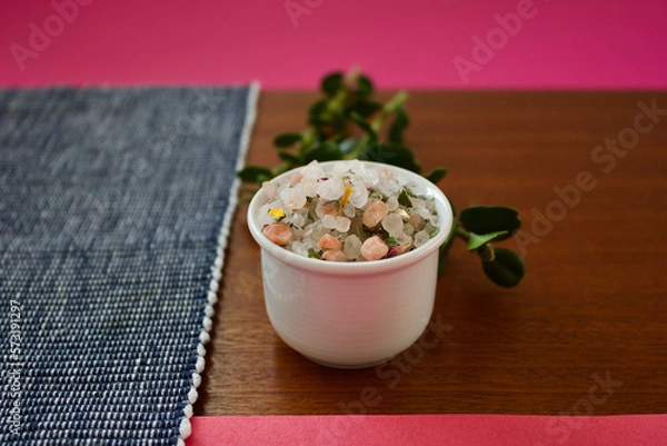 Obraz colorful mountain herb salt in a small white container on a dark wooden plate on a blue white and pink background, copy space