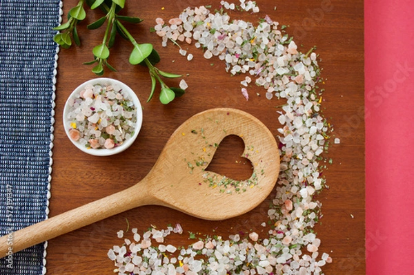 Obraz mountain herb salt in a small white container on a dark wooden plate with a heart kitchen spoon on a blue white and pink background, top view, copy space