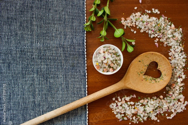 Obraz mountain herb salt in a small white container on a dark wooden plate with a heart kitchen spoon on a blue white and pink background, top view, copy space