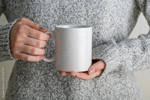 Obraz Female hands holding white mug mockup with blank copy space for your advertising text message or promotional content. Girl in grey sweater holding white porcelain coffee mug mock up, close up