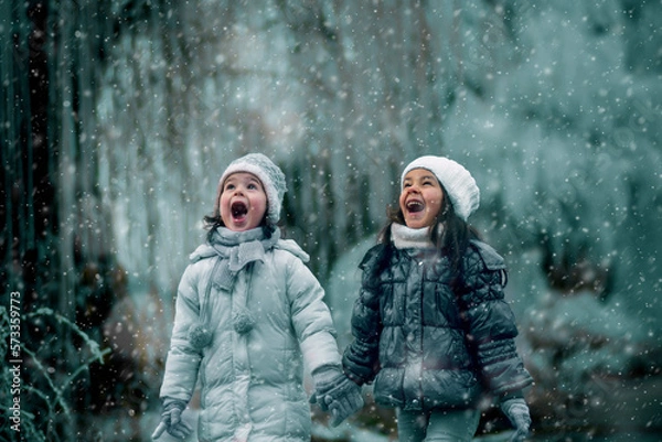Fototapeta Finally snowing. Two girls, warm dressed look at the sky and enjoy in snowflakes. Winter, snowy weather.