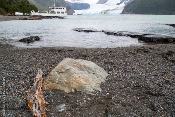 Fototapeta Stone on the shore of the icy lake and in the background view of the glacier and a boat