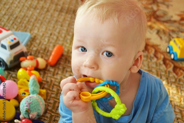 Fototapeta A little boy plays at home with toys. Pulls teether into the mouth