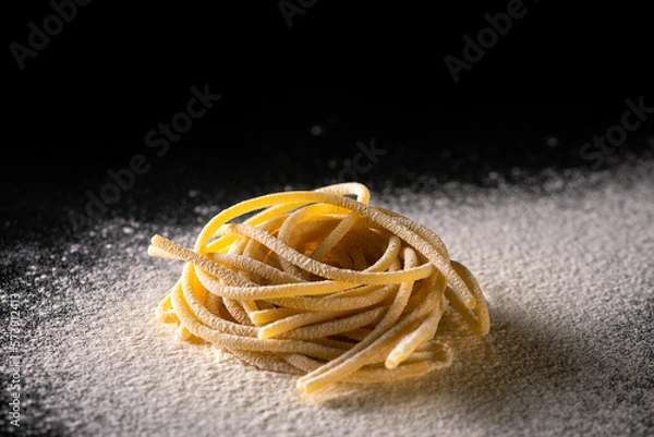 Obraz Uncooked traditional hand - rolled durum wheat pasta Pici of Tuscany, black background and flour in studio light, macro photo of pasta pici and selective focus