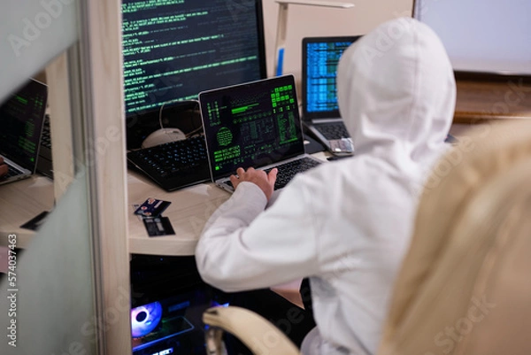 Fototapeta Boy hacker fraudulently use credit card for payment. Internet theft . Man wearing a balaclava and holding a credit card while sat behind a laptop.
