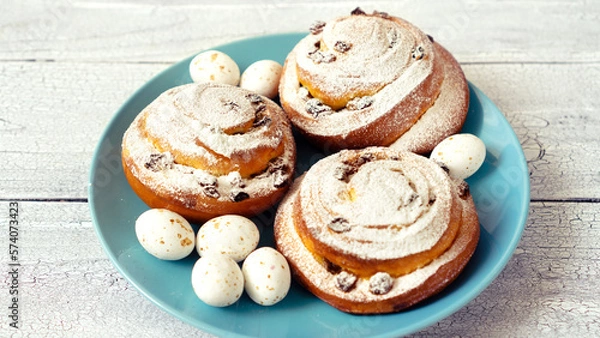 Fototapeta Easter decor with sugar flowers and chocolate eggs with round spiral buns on a blue plate